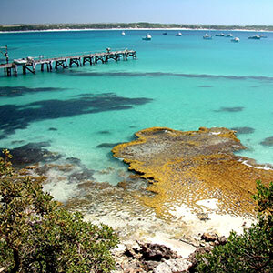 A jetty protudes into the crystal clear turquoise waters of Vivonne Bay surrounded by moored boats