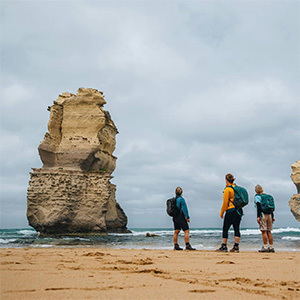 Three people on beach gaze at large rock stack.