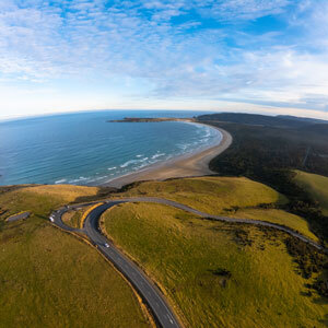An ariel view of a beach with a road wieving through green hills