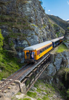 A train travelling in between the mountains with people standing on the back