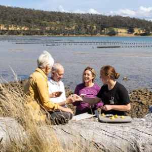 People enjoying fresh oysters by the water with an instructor.
