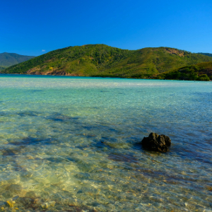 Clear tropical waters along a sandy beach with scattered rocks.