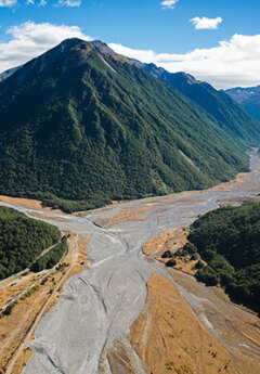 An aerial view of a wide, braided riverbed with a mountain in the background.