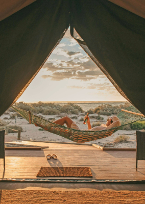 A person relaxes in a hammock on a deck by a beach.