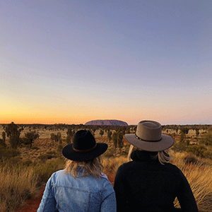 Two guests looking over Uluru in the distance at sunset