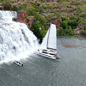 Catamaran sailing near a large tropical waterfall.