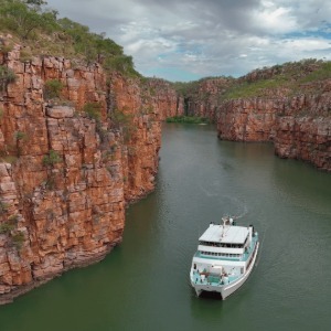 A cruise ship navigates a river gorge with red cliffs.