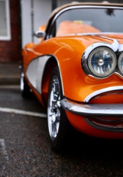 A bright orange classic car with chrome details sits on a wet street.