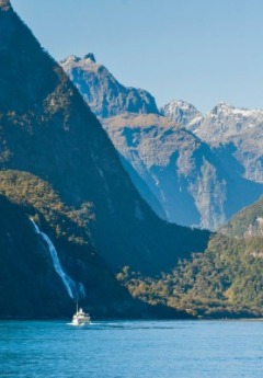 A small boat cruises on a fjord past a waterfall and mountains.