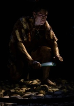 A male Māori warrior crouches, holding a green mere