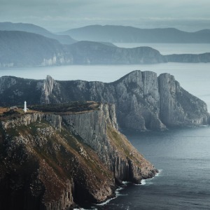 A lighthouse on a dramatic cliffside overlooking the water and distant mountains.