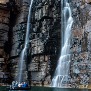 A small boat with people approaches a powerful dual waterfall.