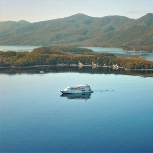 A ship sails across a calm blue lake between two landmasses.