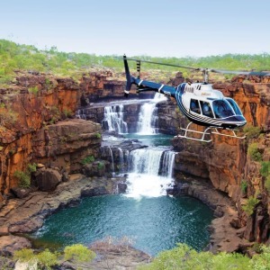 A helicopter hovers next to a magnificent, tiered waterfall in a rocky gorge.
