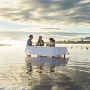 Three people are dining at a table set in a lake.