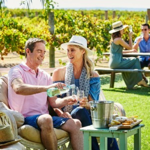 Couple laughing, enjoying white wine and cheese platter outdoors.
