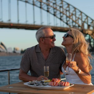 A couple enjoying a seafood platter on a boat under the Sydney Harbour Bridge