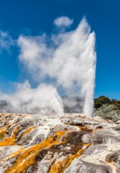 The Pohutu Geyser erupts high into the air over the colourful geothermal rock.