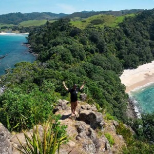A hiker stands on a rocky outcrop overlooking two secluded, beautiful beaches.