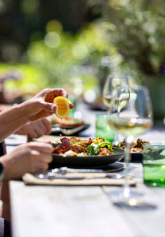 A lemon being squeezed over a freshly cooked meal with a glass of wine