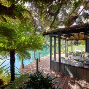 Covered deck by turquoise water with lush ferns and tropical foliage.