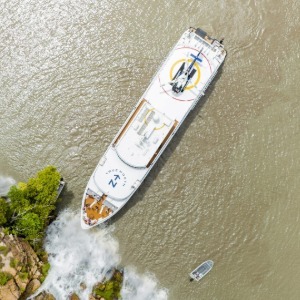 Top-down view of a ship's bow touching a waterfall's base.
