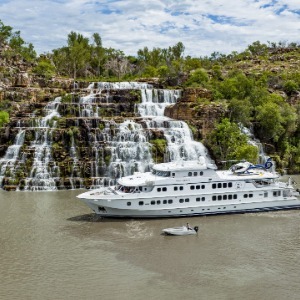 Large white cruise ship floating past a wide, terraced waterfall.
