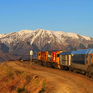 TranzAlpine train heading towards snowcapped mountains on sunny day