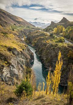 A scenic view of the Kawarau River Gorge with a road in the distance.