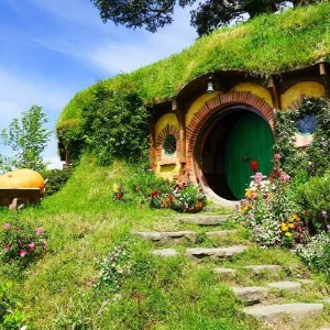 A colourful Hobbit Hole with a round green door and stone steps sits on a grassy hill.