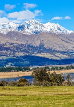 Snowy mountains rise over rolling foothills and a lake on a sunny day.