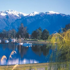 Boats float on a calm lake reflecting dark mountains with snow-capped peaks.
