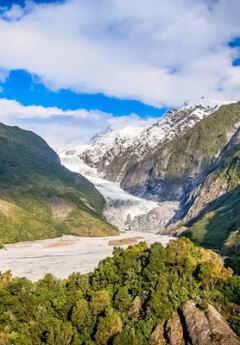 A glacier sits between snowy capped mountains