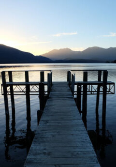 A wharf stretches out over Lake Te Anau while the sun sets behind the surrounding mountains