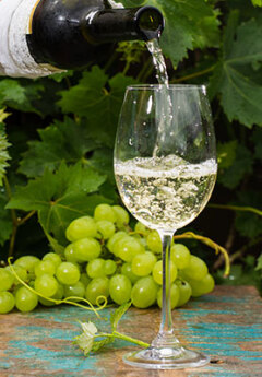 White wine poured into a glass of white wine and green grapes on a table