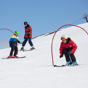An instructor coaches skiers through hoops on the white snow at Coronet Peak with contrasted blue skies