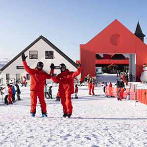 Two Cardrona staff in red wave back at the camera looking back at the base building