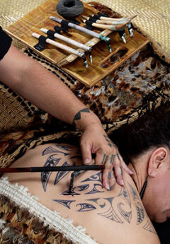 Maori woman tatooing another woman with Maori symbols