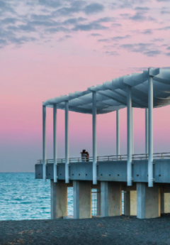 Couple standing at the end of a pier in front of a pink sunset