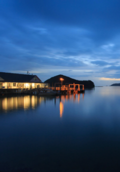 Lit boathouse and pier at dusk on calm water