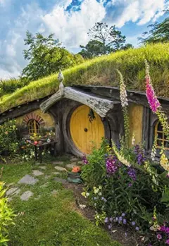 Yellow door of a Hobbit house and colorful flowers in the front