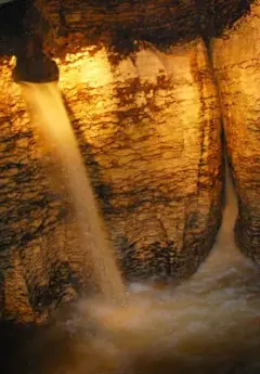 Two waterfalls appear out the side of a rockwall inside the Te Anau Glow Worm Caves