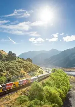 TranzAlpine Train heading towards the mountain range on a sunny day