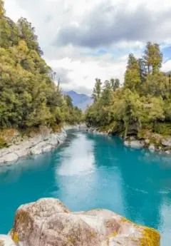 Bright Blue water with grey rocks and trees surrounding