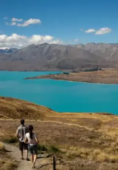 Couple walking by turquoise lake and mountains.