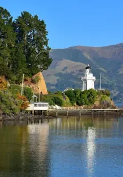 A lighthouse and wharf sit on a hill and reflect onto the lake below