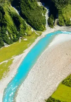 A turqouise river runs alongside a mountain covered in bush