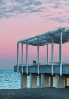 Couple standing at the end of a pier in front of a pink sunset